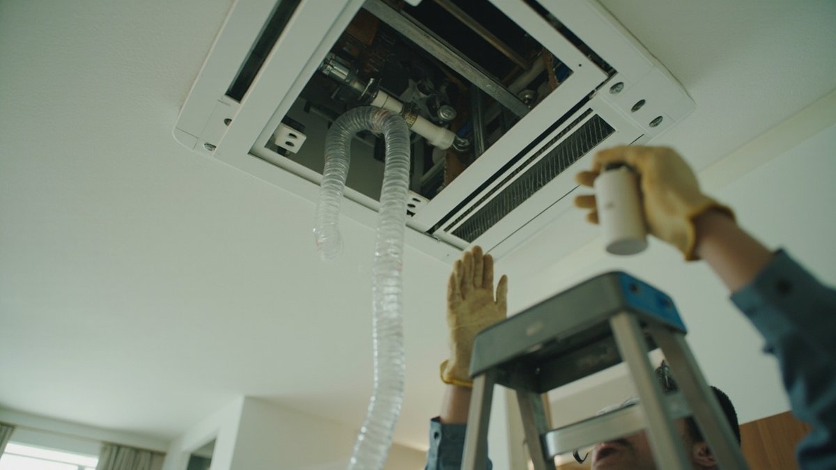 Technician's hands holding a condensate pump under an opened ceiling cassette aircon