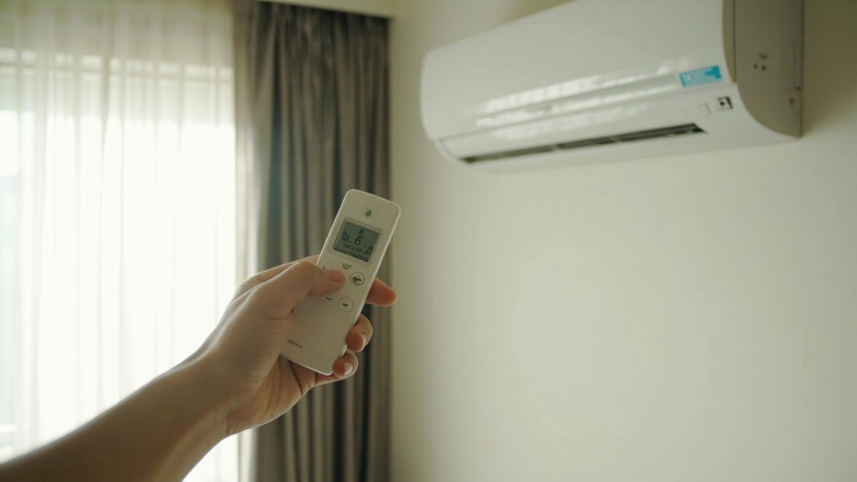 手持冷气遥控器对着卧室里的壁挂式分体冷气
