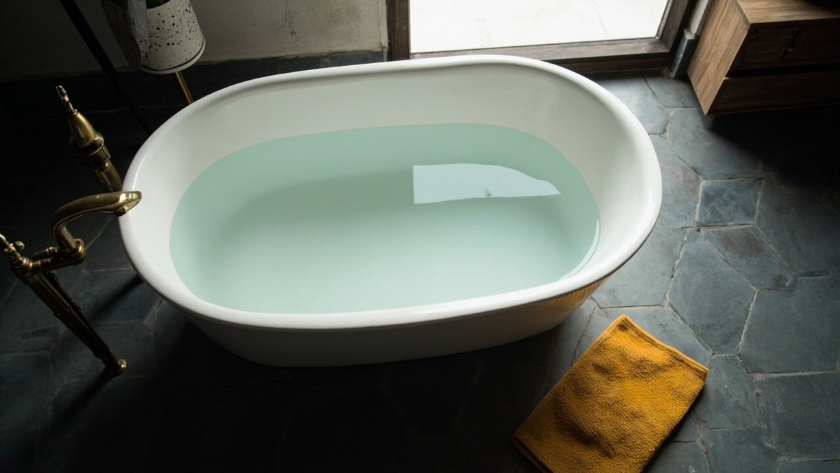 Top-down view of a freestanding oval bathtub on dark hexagon floor tiles with a brass tap