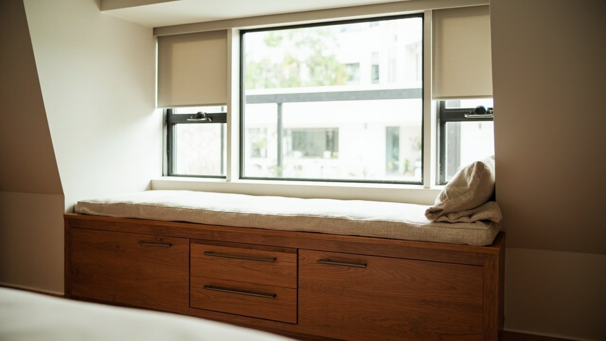 Condo bay window turned into a built-in seat with drawers and a cushion, roller blinds on the windows