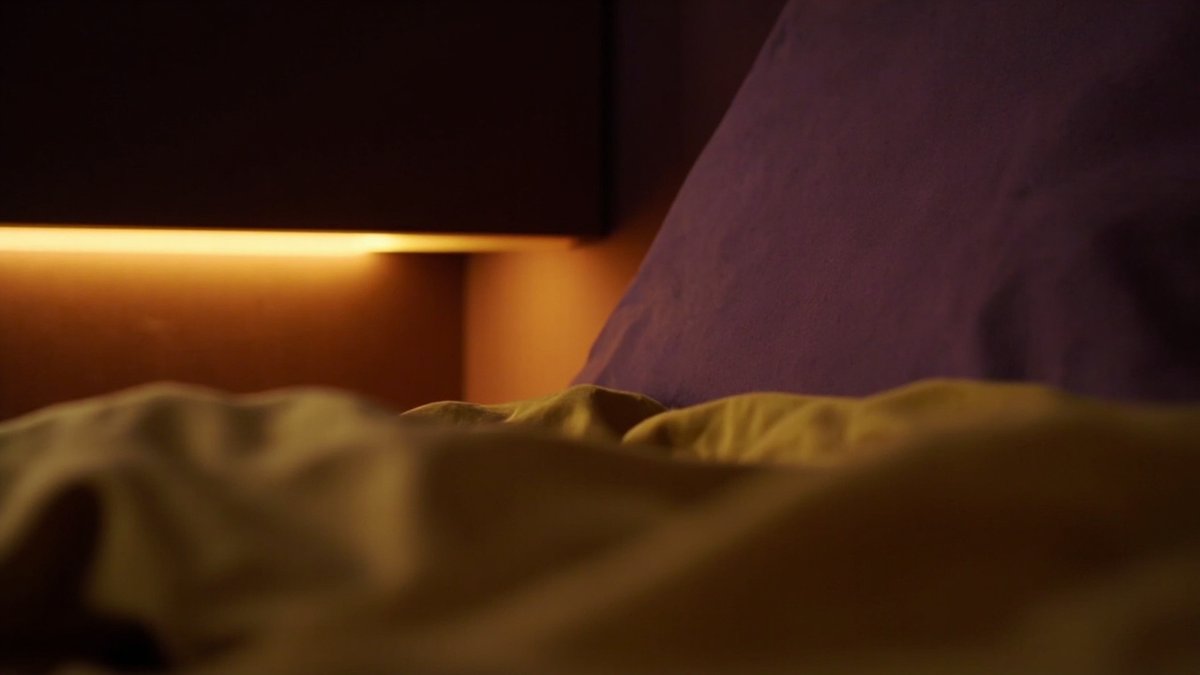 View from the pillow up to a bedroom ceiling recess with a warm light line above a plum headboard wall