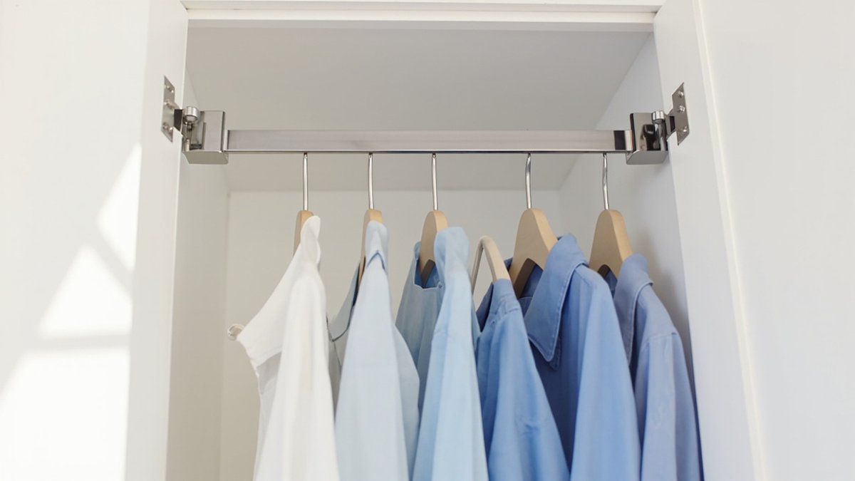 Illustrative concept design: white wardrobe top section with a chrome pull-down rail on hinged side brackets holding blue and white shirts