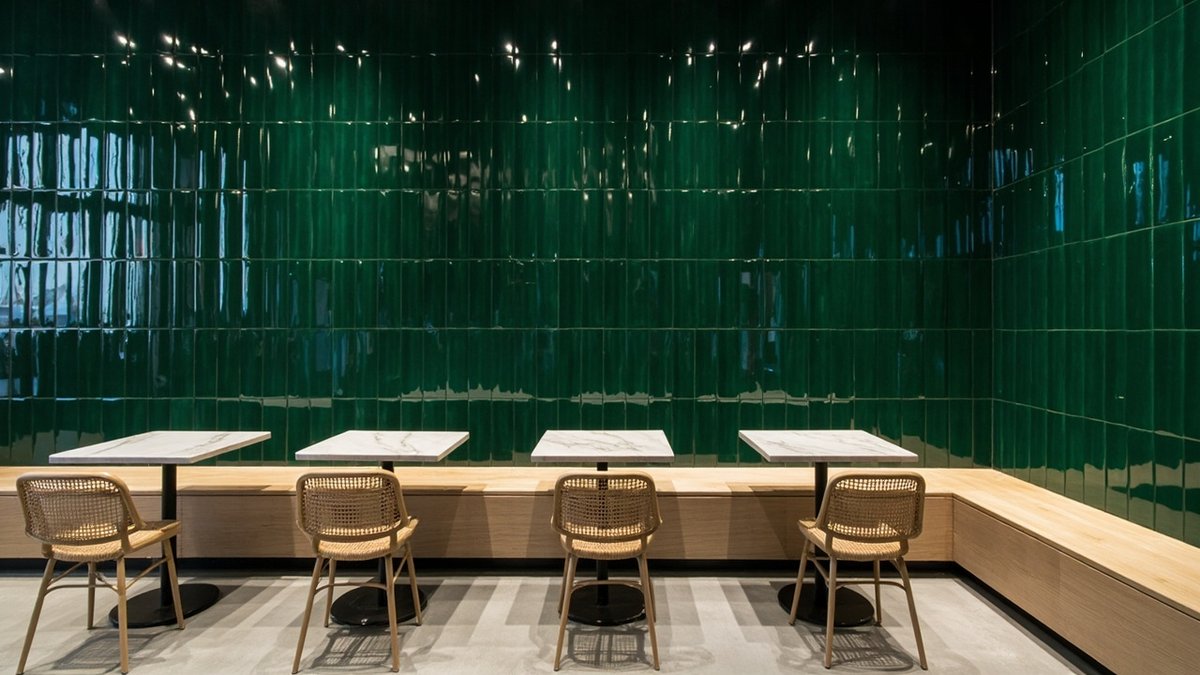 Illustrative concept design: cafe corner with a glossy deep green tiled wall behind an oak bench and round tables