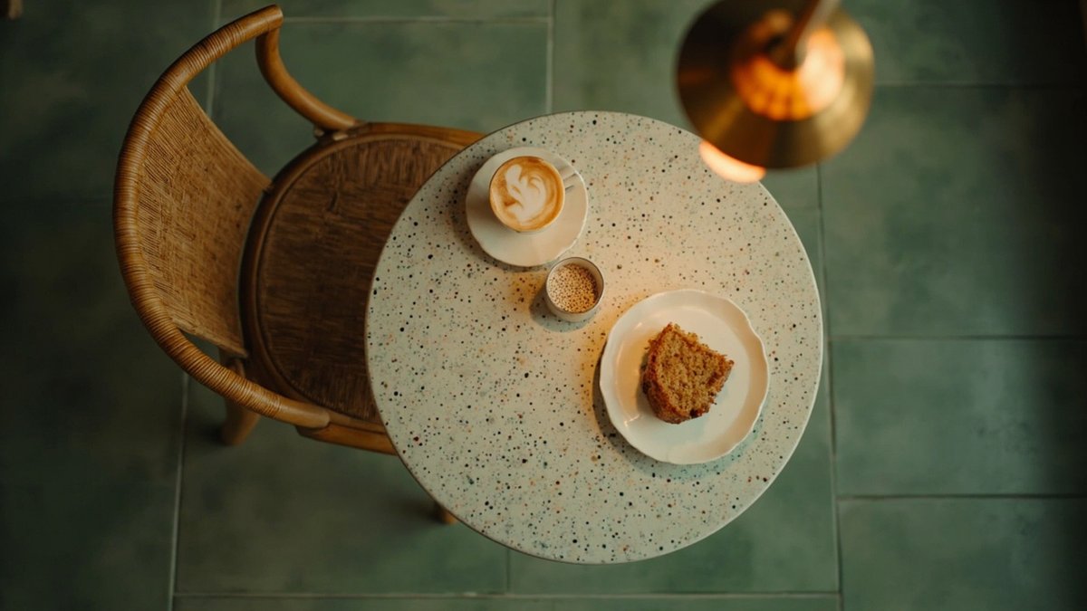 Overhead view of a terrazzo cafe table with coffee under a brass pendant on a sage-green floor