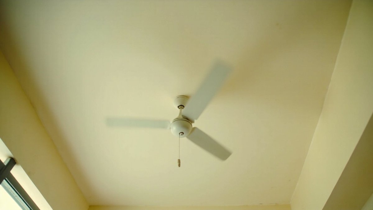 White three-blade ceiling fan with a pull cord, seen from below with its blades spinning in a blur