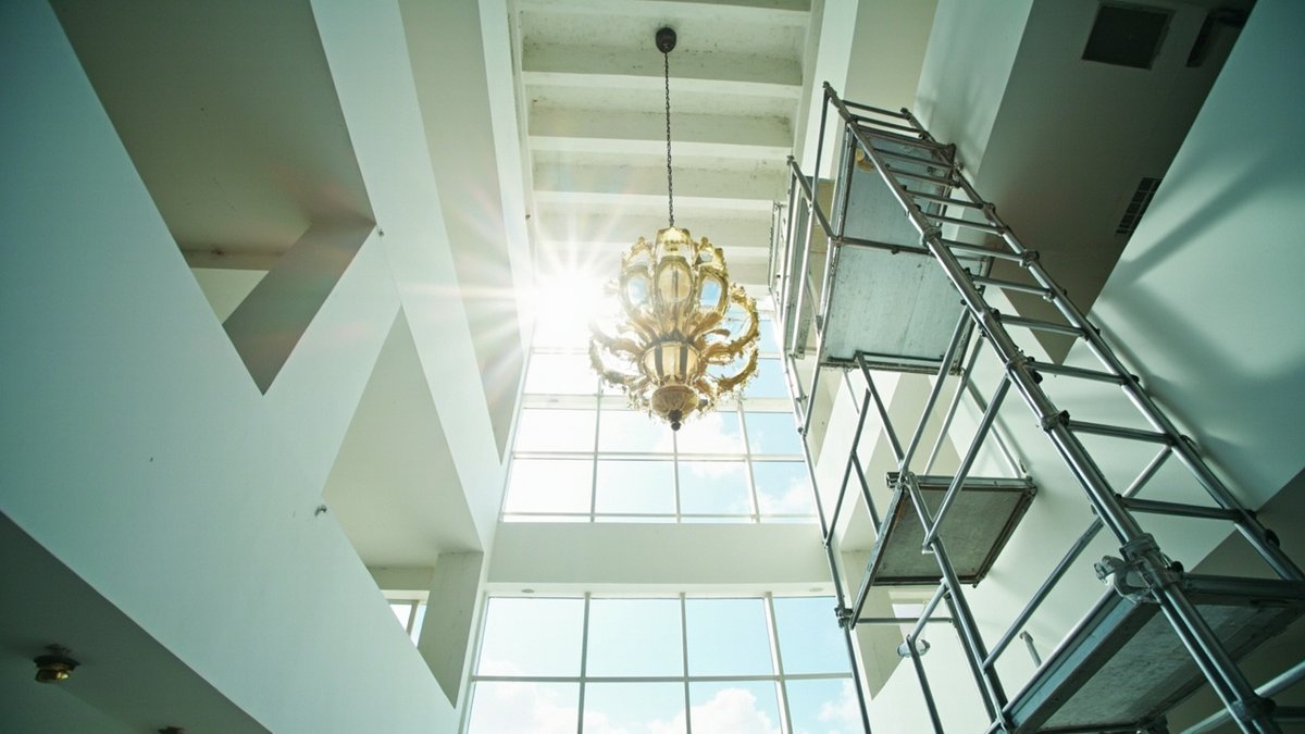 A tiered chandelier hanging on a long chain in a double-height hall with an aluminium scaffold tower beside it