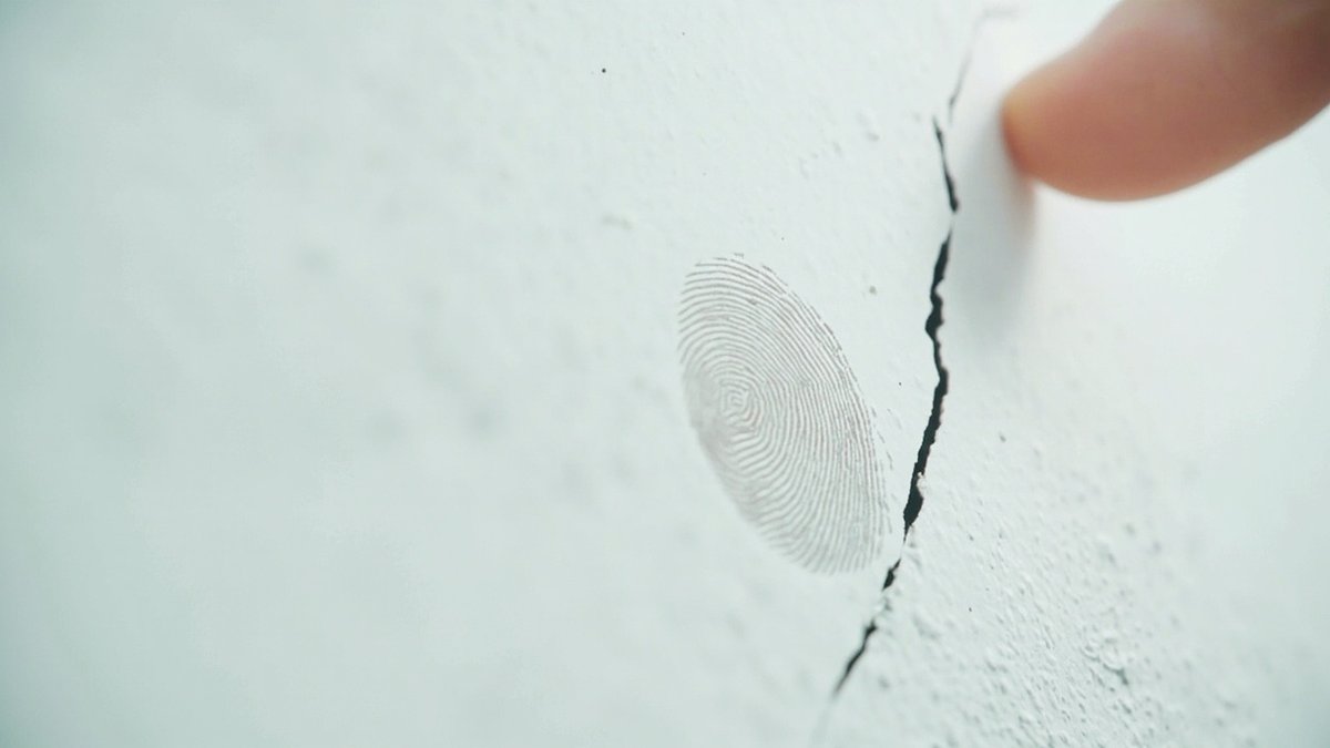 A macro shot of a hairline wall crack shows a defect covered under the defect liability period.