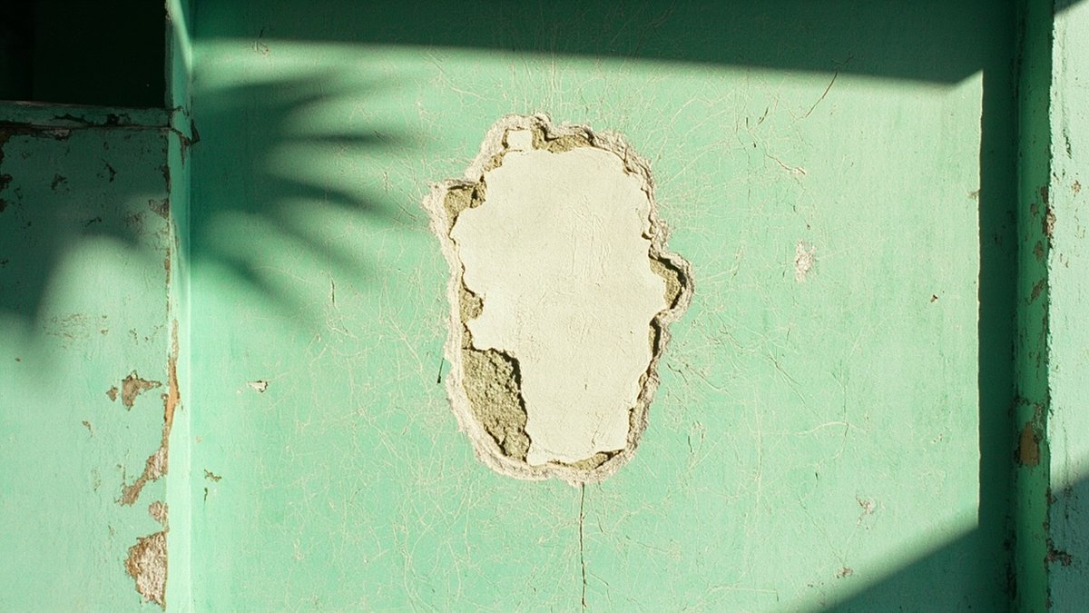Faded, chalky exterior wall paint with fine crazing cracks on a terrace house
