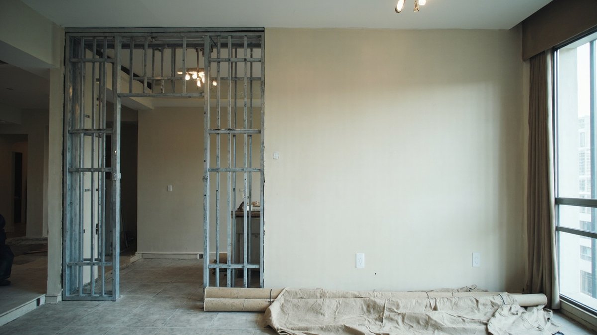 Bare metal stud frame for a false wall with a doorway opening, in an unfinished room beside a tall window