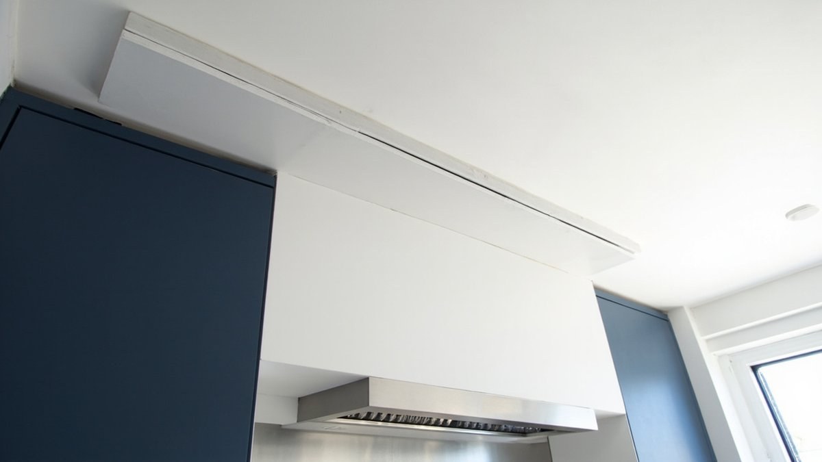 Illustrative concept design: white plaster box enclosing a cooker hood duct up to the flat ceiling between navy tall cabinets