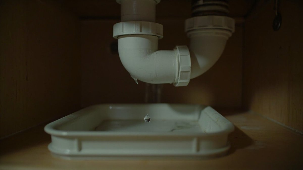 Water droplet forming at a trap nut under a kitchen sink, with a tray below