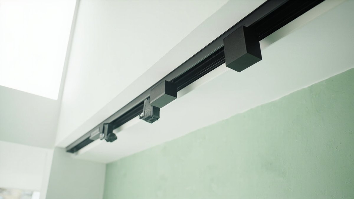A black magnetic track rail recessed into a white ceiling with spot heads and a linear module clipped on