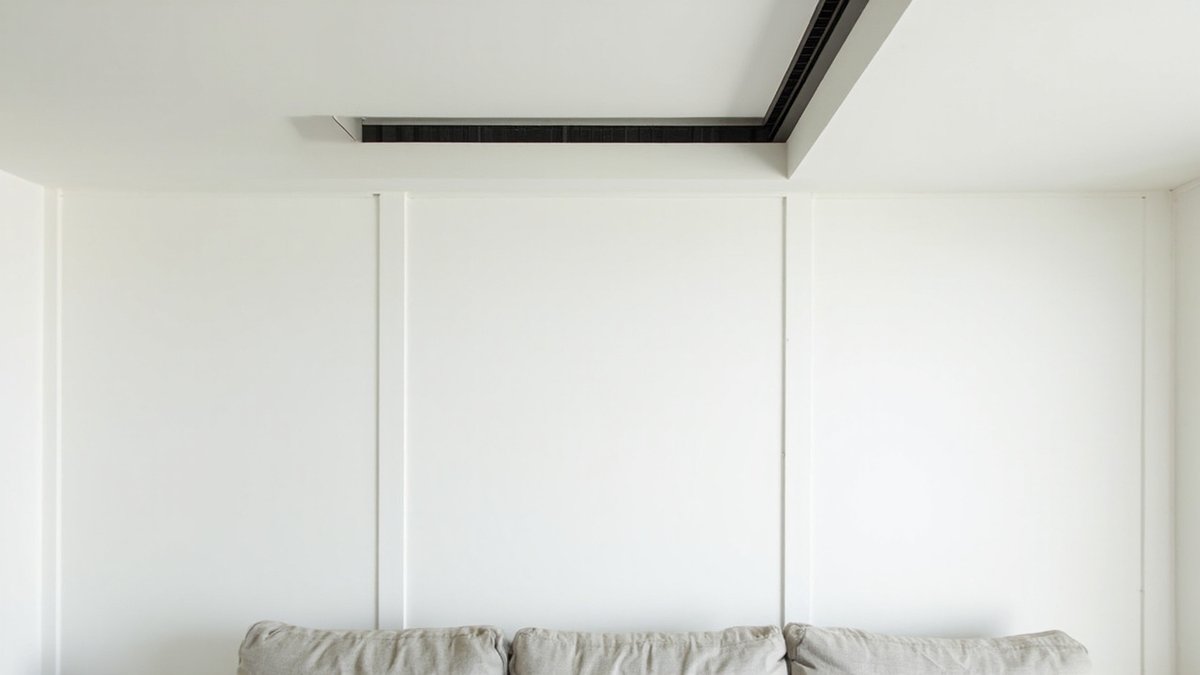 Ilustrasi konsep reka bentuk: gril aircond linear gelap yang panjang dalam alur siling putih di atas dinding berpanel dan sofa linen
