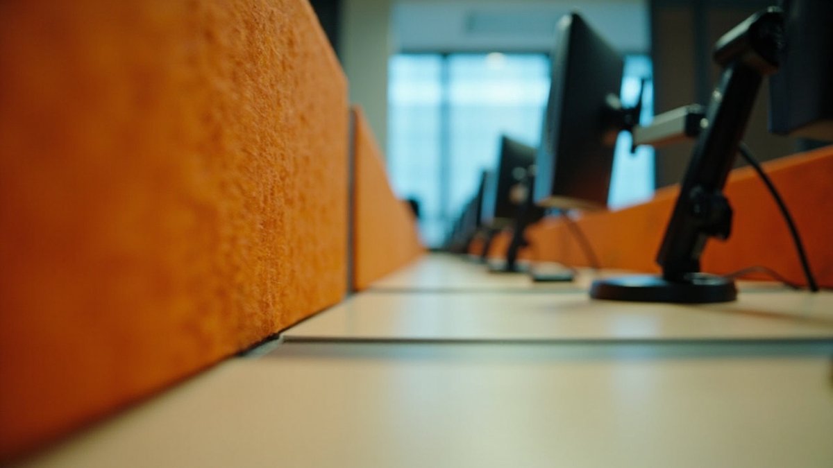 Close-up of an orange felt desk screen along a row of office workstations