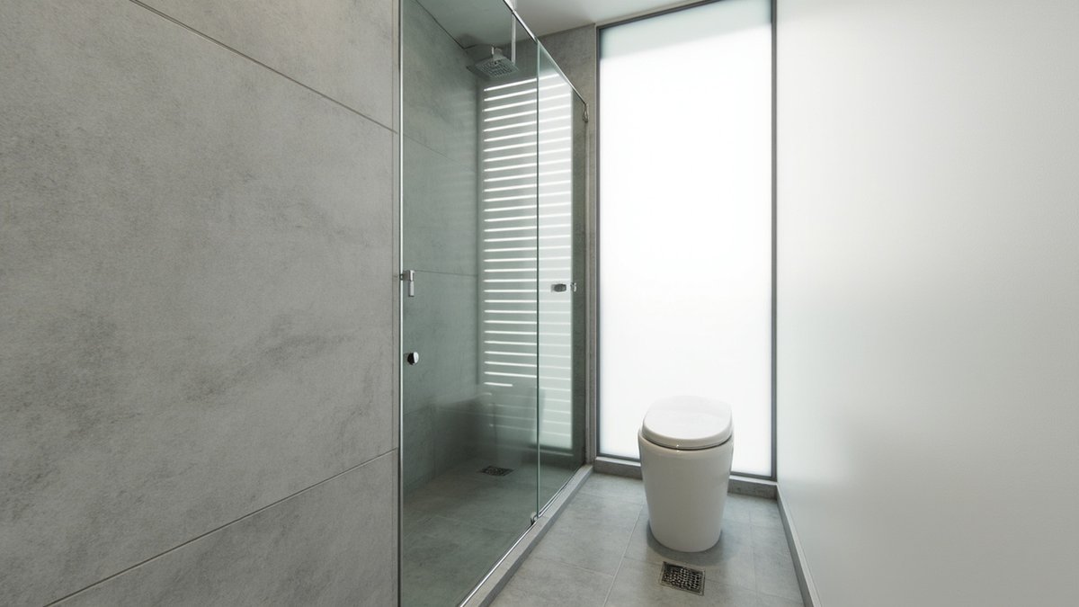 Illustrative concept design: grey large-tile bathroom with a sliding glass shower, a tall frosted window, a seated toilet and floor traps