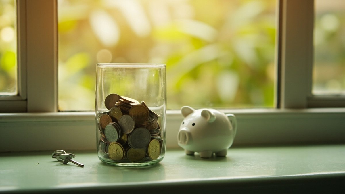 Savings jar of coins, a piggy bank and a house key saved up for a property down payment