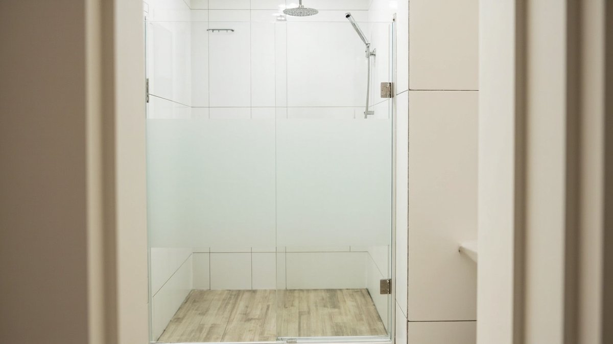 Illustrative concept design: frameless glass shower screen with a wide frosted privacy band seen through an ensuite doorway