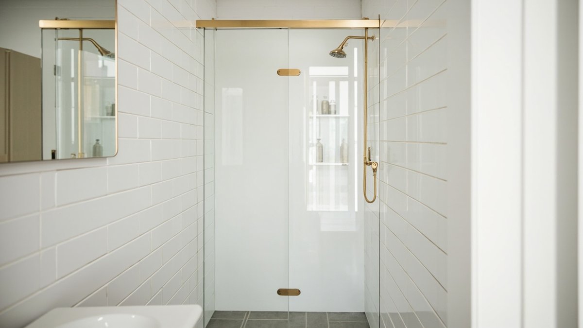 Illustrative concept design: frameless glass shower door with brushed gold hinges closing a white subway-tiled alcove