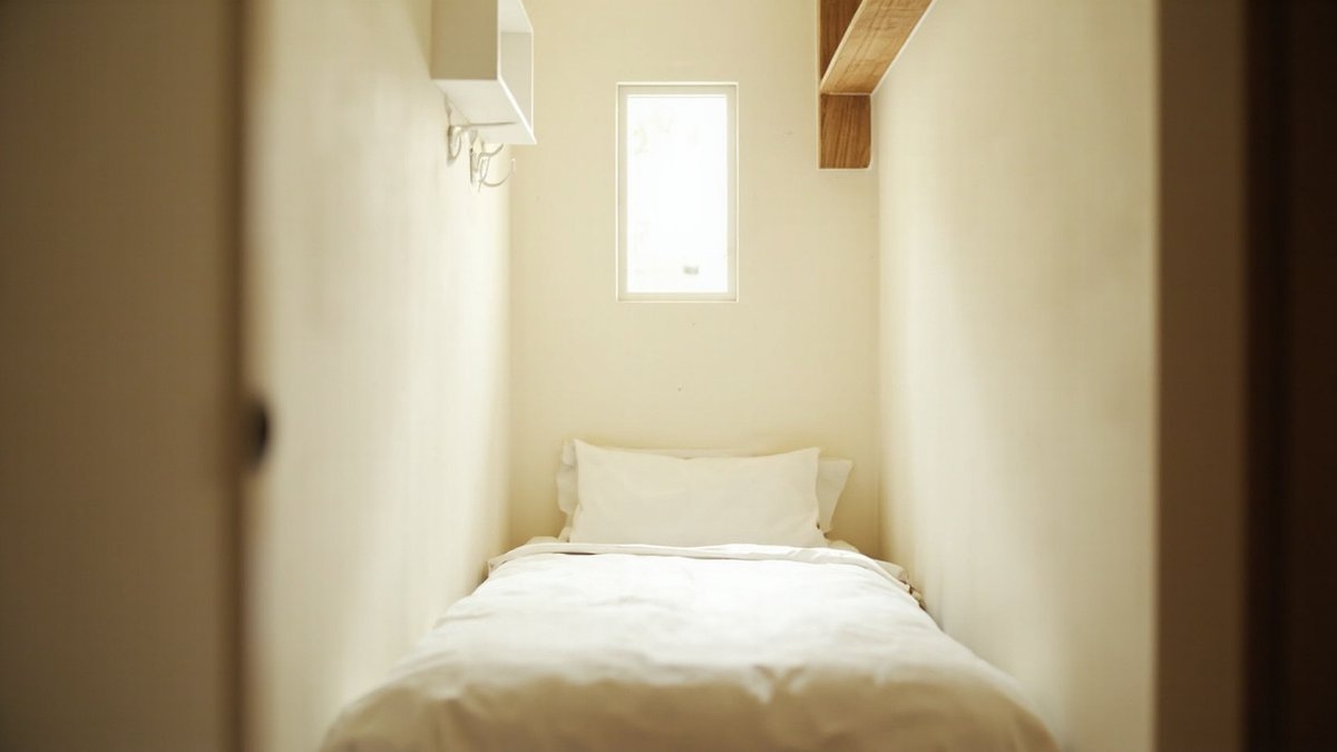 Illustrative concept design: narrow box room with a single bed under a small window, a white wall cubby with hooks and an oak shelf