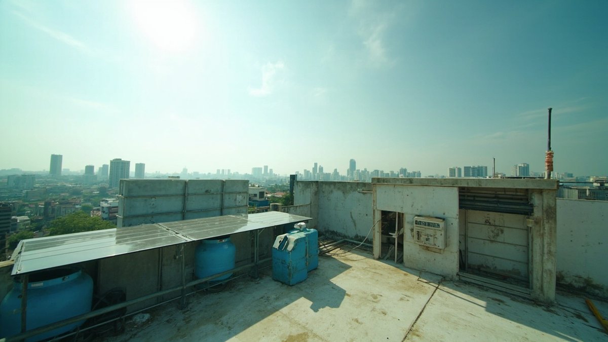 Short row of solar panels mounted above blue water tanks on a flat rooftop, with a hazy city skyline behind