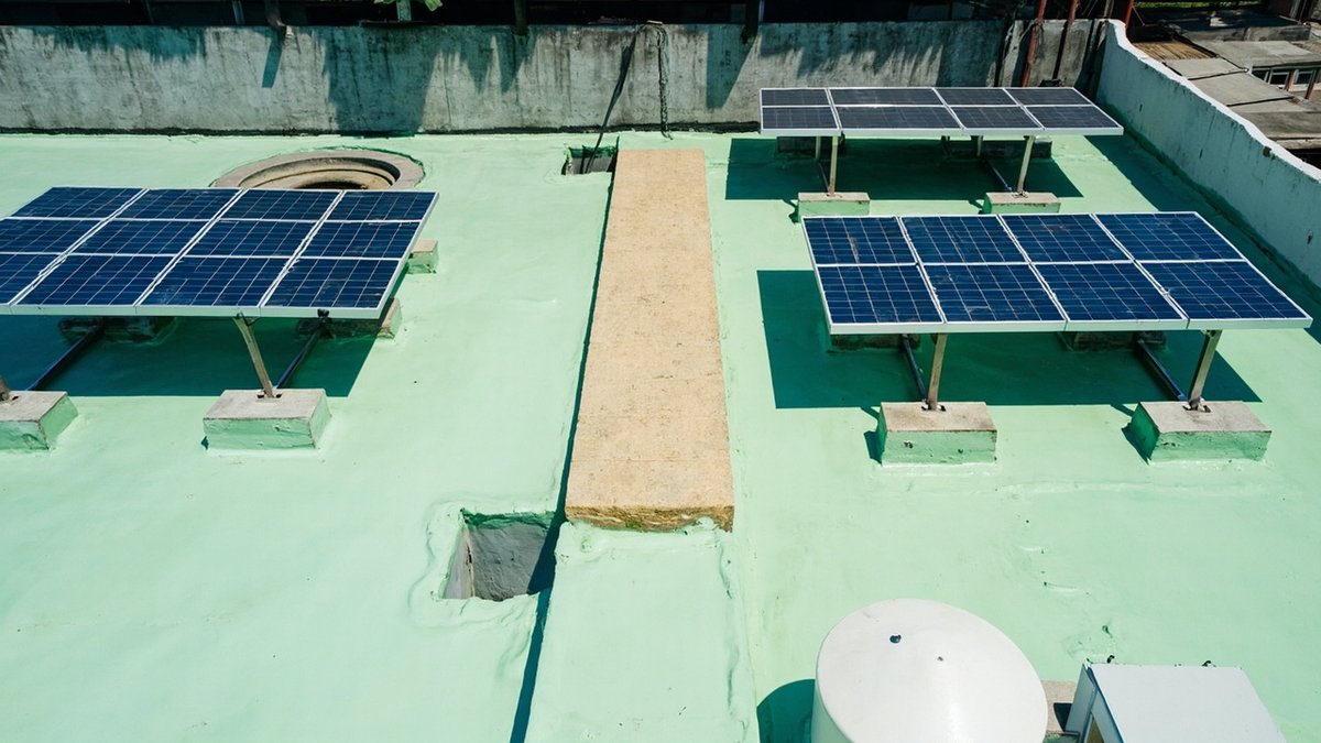 Barisan panel solar condong rendah atas rangka ballast di bumbung konkrit rata yang baru disalut, dengan laluan jelas ke saluran keluar