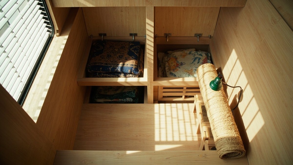 Overhead view of a raised oak tatami platform with lift-up storage lids open in a small bedroom
