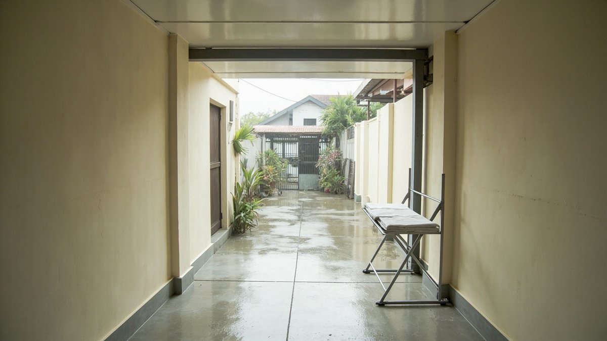 Illustrative concept design: insulated off-white panel roof on a steel beam over a narrow terrace back yard on a rainy day, folding rack below