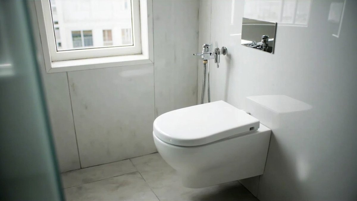 White wall-hung toilet with a flush plate and bidet spray in a tiled bathroom
