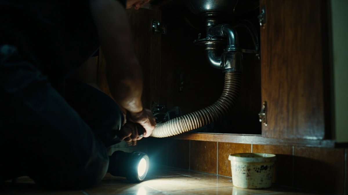 Plumber tightening a new sink trap and hose under a kitchen sink