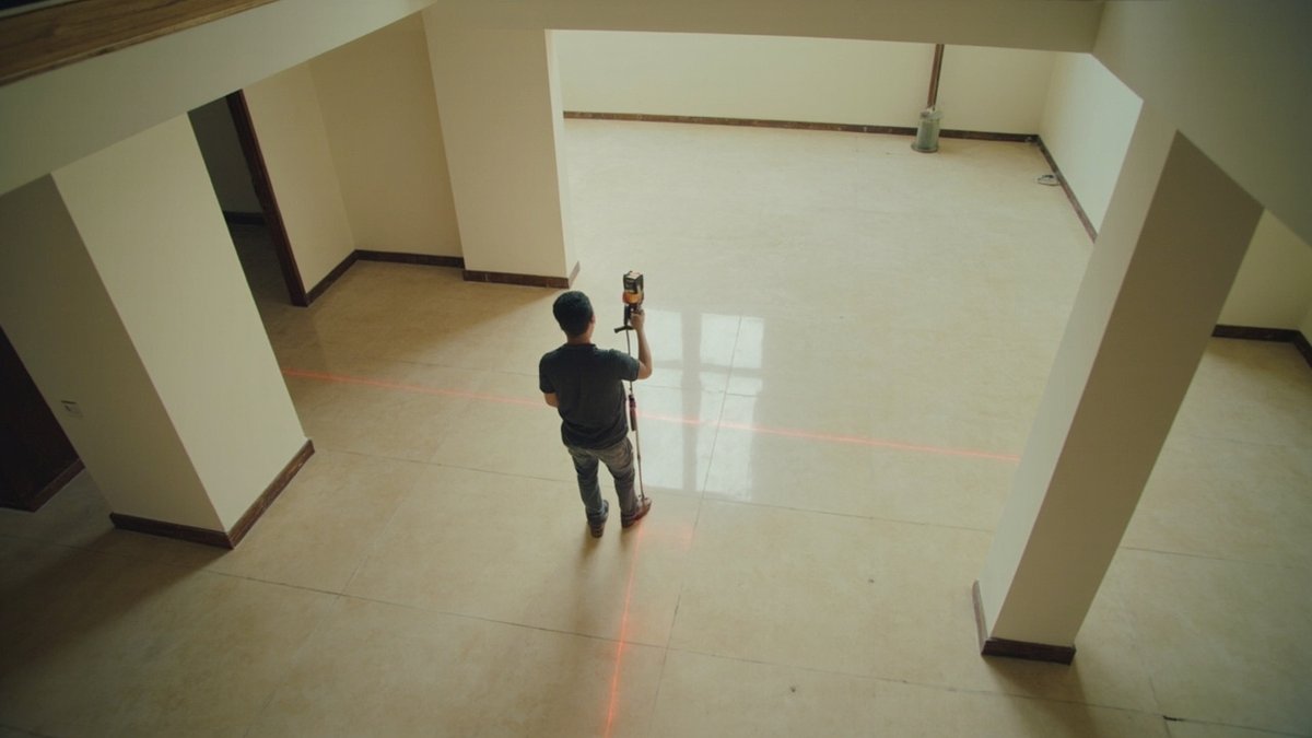 Kontraktor mengukur ruang tamu kosong menggunakan meter laser untuk menganggarkan kos renovasi