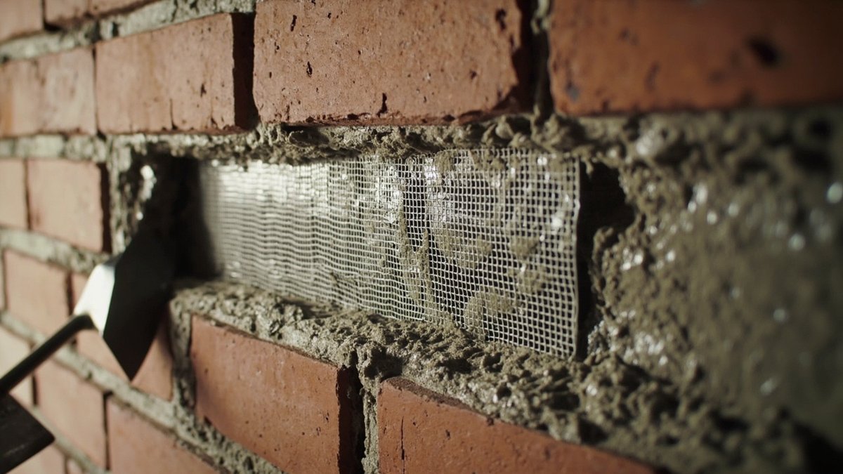 Freshly filled wall chase bridged with fibreglass mesh in wet mortar, the buried conduit visible at the edge