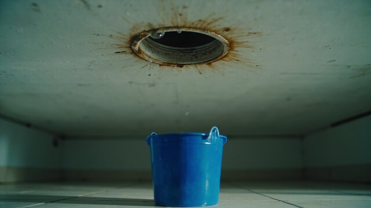 A water drop falling from a switched-off downlight with a brown stain ring into a pail below