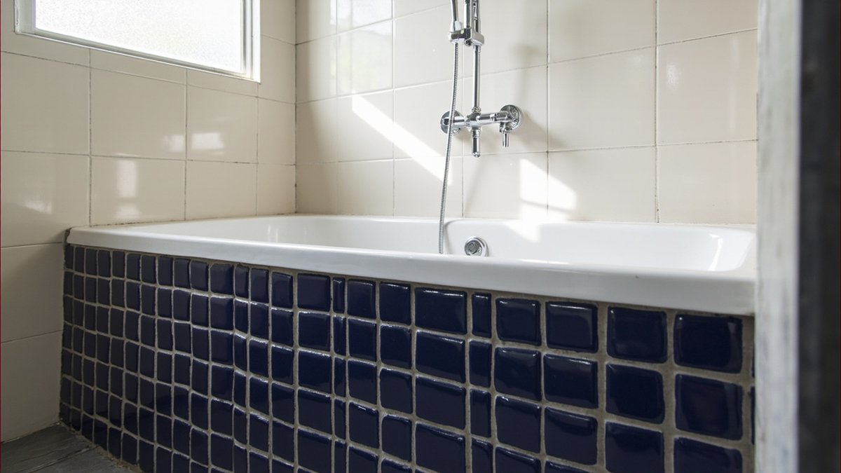 Illustrative concept design: built-in white bathtub with a small navy blue tiled apron in a cream tiled terrace bathroom