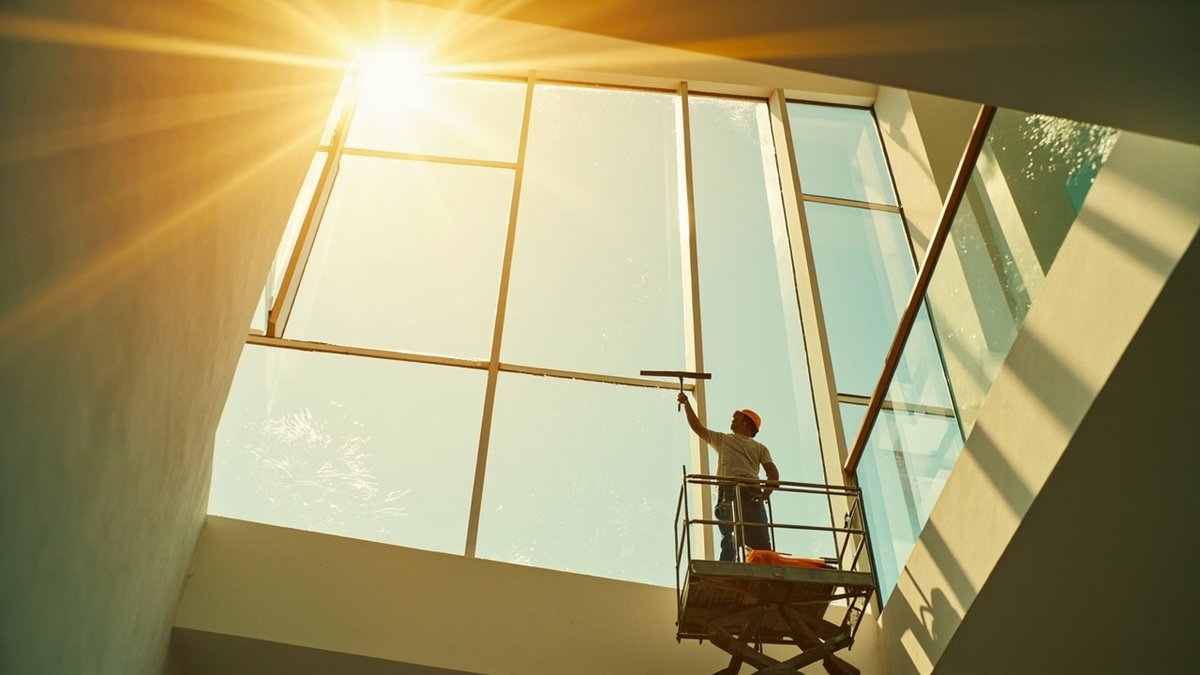 Cleaner on an access platform cleaning a high staircase window in a terrace house